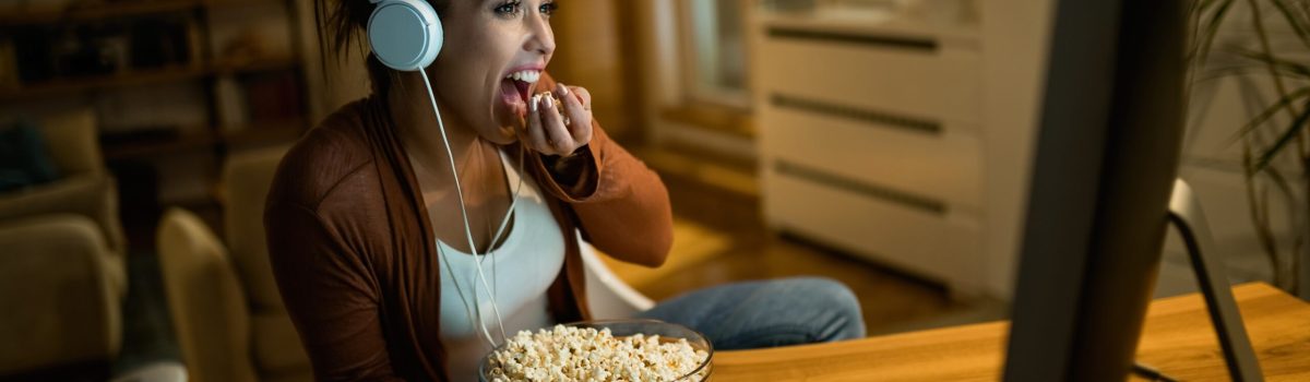 Young woman eating popcorn while watching movie on desktop PC at home.